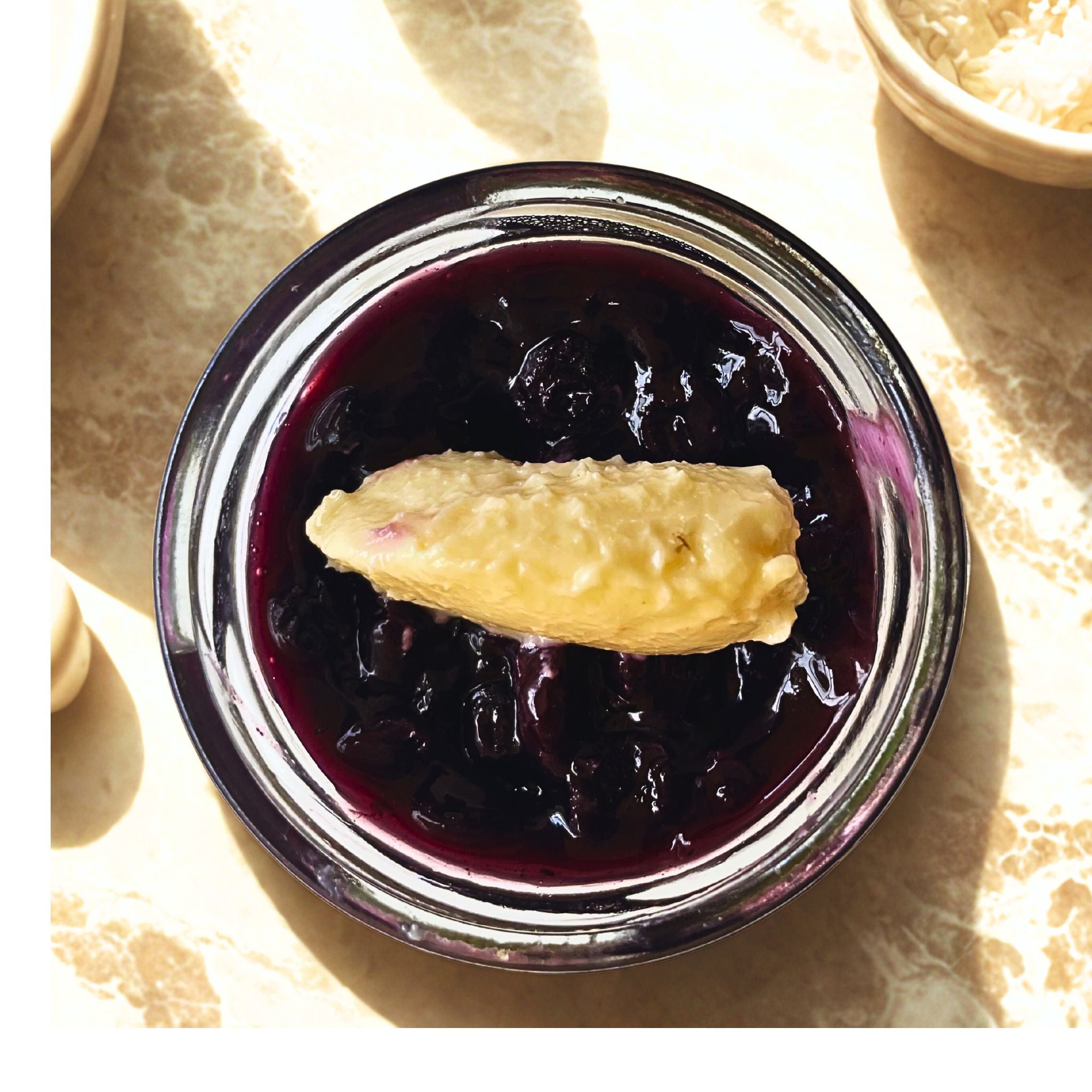 Top view of blueberry cheesecake in a jar, topped with whole blueberry compote and a biscotti stick, styled on a stone surface.