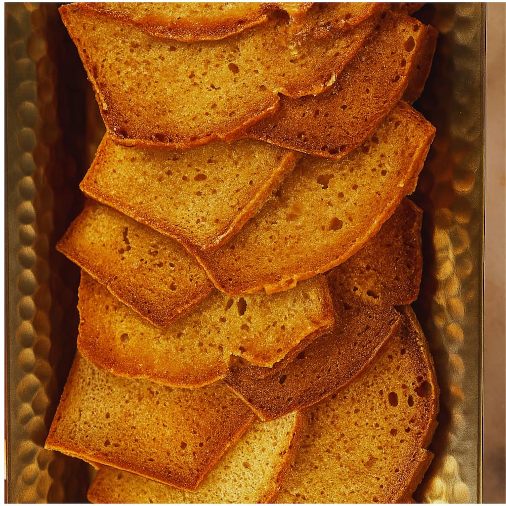 Thin golden slices of crispy butter cake chips stacked on a gold tray, a unique sweet snack by Seven Rivers Cheesecake.