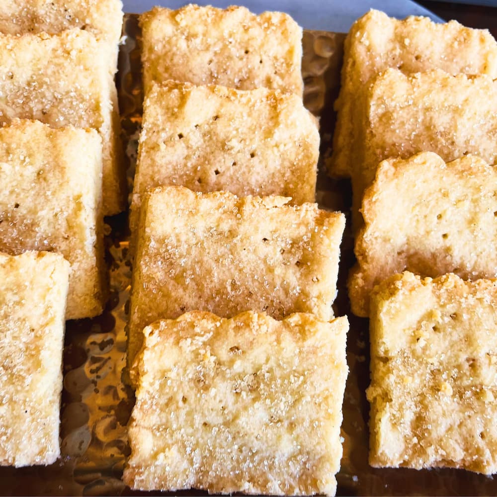 Buttery almond shortbread squares arranged on a gold tray, showing a crumbly texture and golden edges.