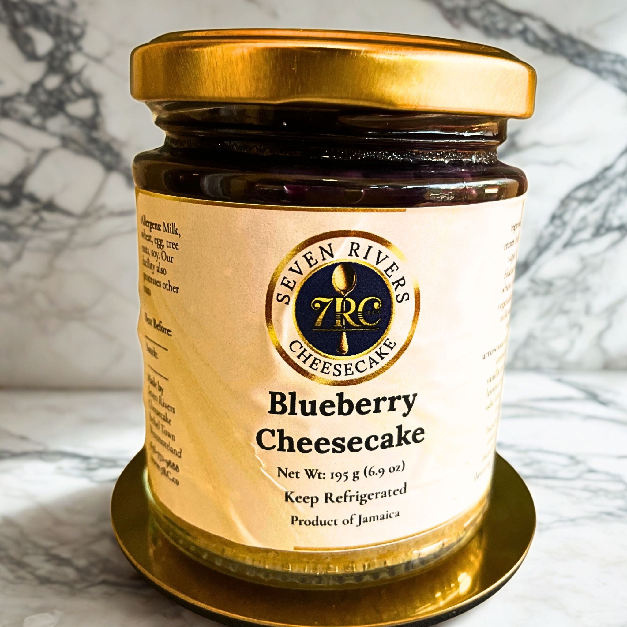 Label view of Seven Rivers Blueberry Cheesecake jar with deep purple topping, gold lid, and marble background.