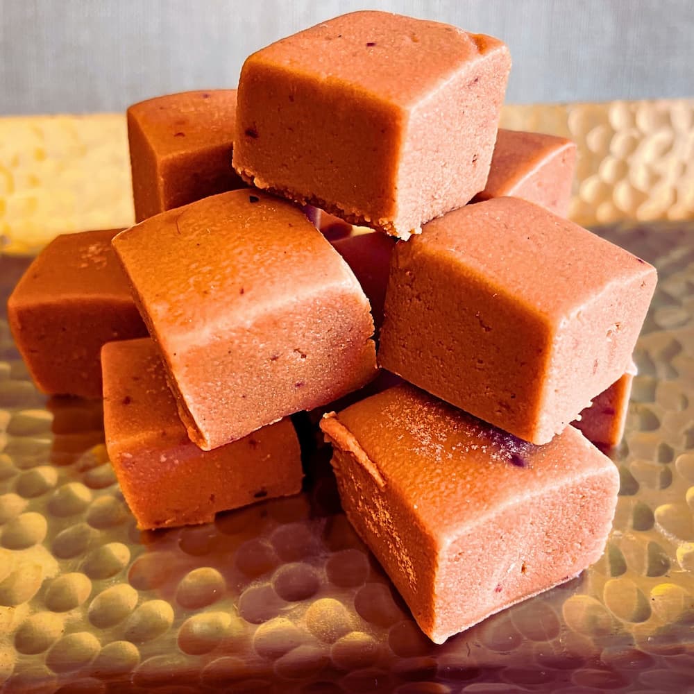 Cubes of raspberry sweet milk fudge stacked on a golden hammered tray, with a smooth, creamy texture and soft pink hue.